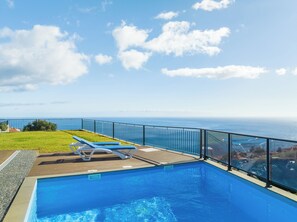 Relax by the ocean with a clear view from our pool area, surrounded by lounge chairs and a wooden deck.