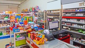 A retail store with shelves stocked with various products, a computer monitor, and a cash register.