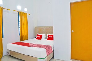 Una cama bien hecha con una colcha de diseño rojo y blanco, dos almohadas rojas y un cabecero tapizado en color beige.