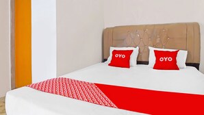 A hotel room with a bed, two red pillows with the word "OYO" on them, a white bedspread, and a red and white patterned throw blanket.