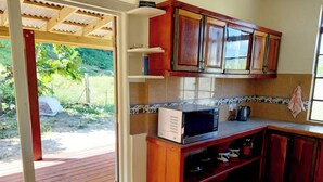 A kitchen with wooden cabinets, a microwave, and a tiled backsplash. - Comfortable, local home with A/C and private verandah (Calibishie)