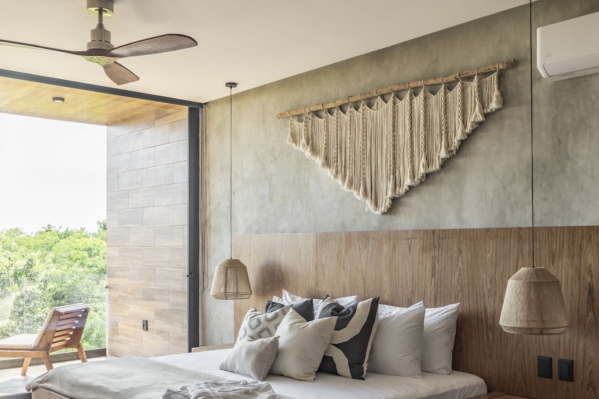 A modern bedroom with a large bed, wooden headboard, and a view of greenery outside.