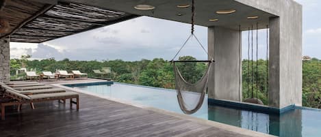 A modern outdoor pool area with wooden deck, lounge chairs, and a hanging chair.