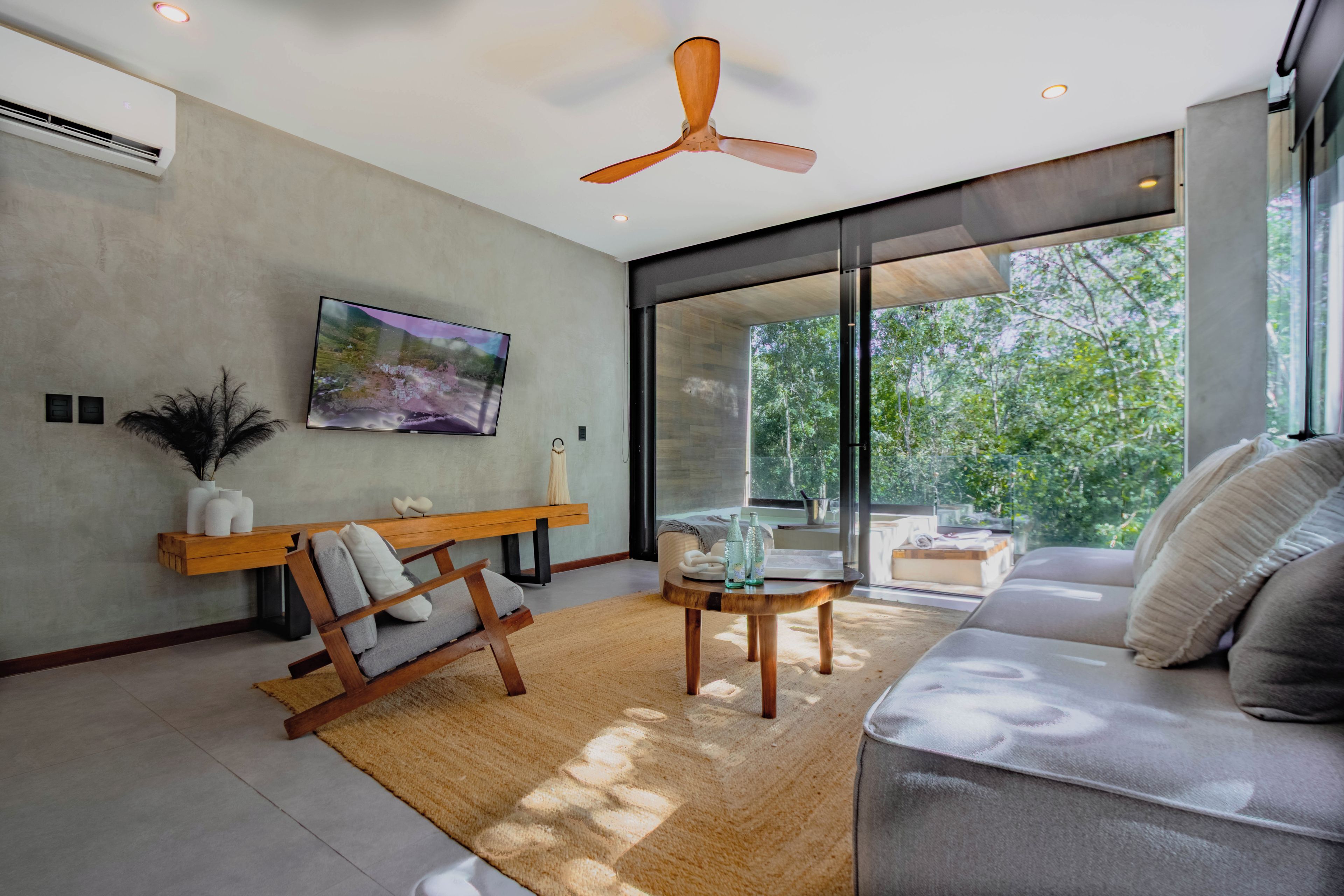 A modern living room with a sofa, a wooden bench, a flat-screen TV, and a ceiling fan.