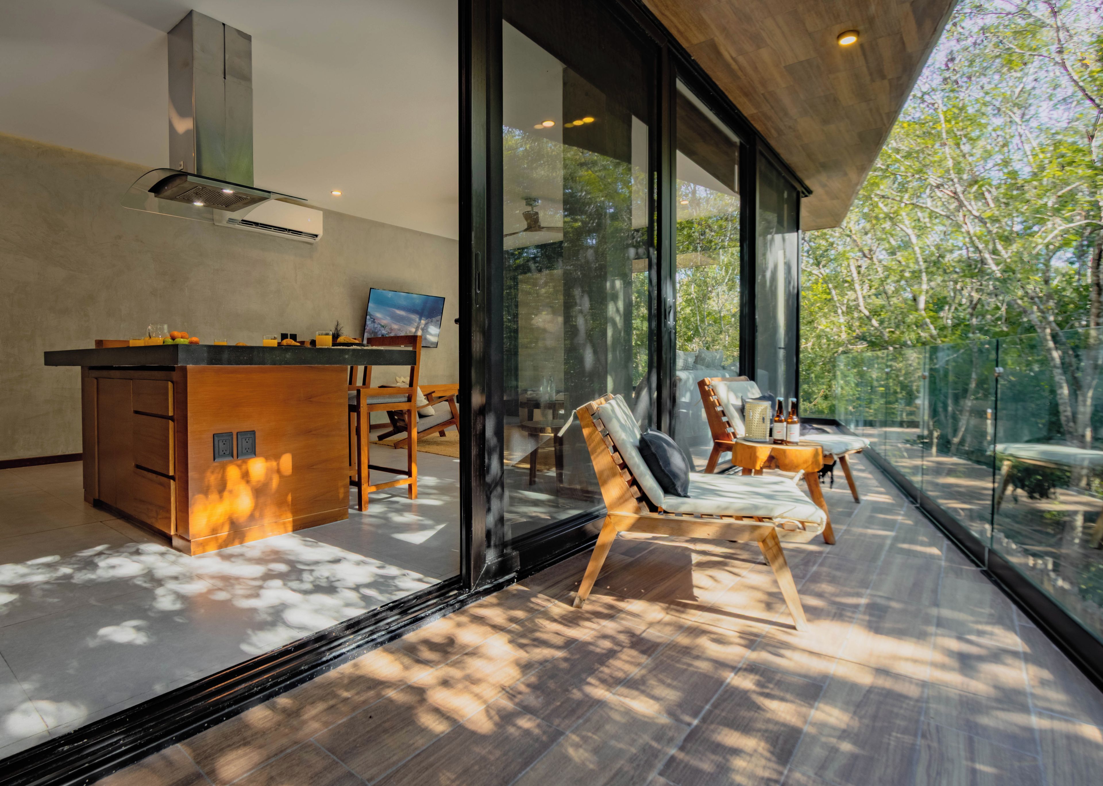 Une cuisine moderne avec un îlot central en bois, un coin repas doté d’une table en verre et un espace détente avec des fauteuils.