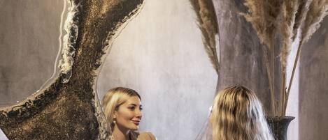 Una mujer de pie frente a un espejo grande con un marco circular, reflejando su imagen.