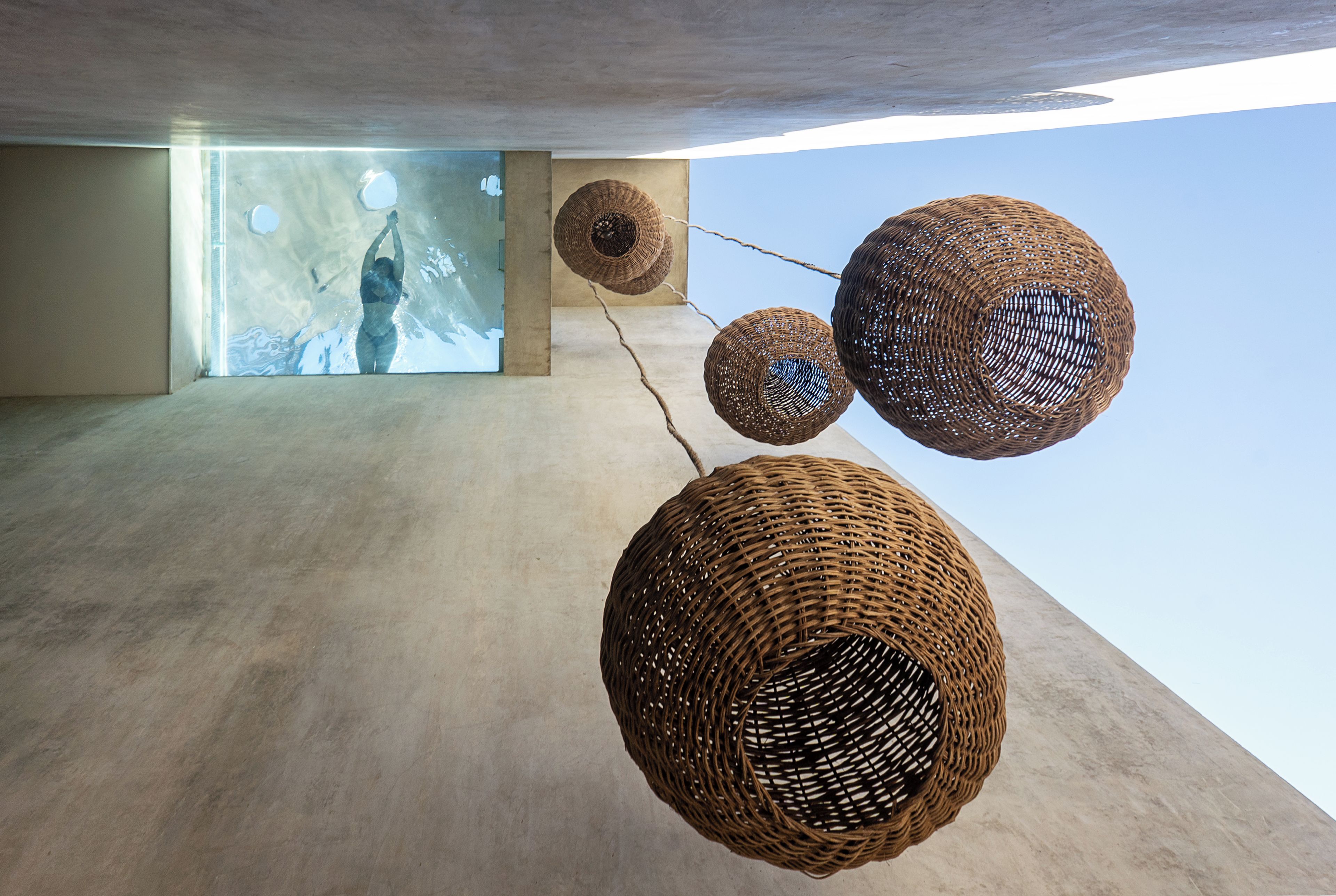 A modern interior with concrete walls and a large window. There are three spherical wicker structures hanging from the ceiling.