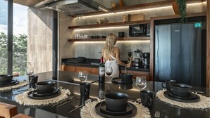 A modern kitchen with a central island, equipped with black bowls and wine glasses, and a woman preparing a drink. - Xambé  (Tulum)