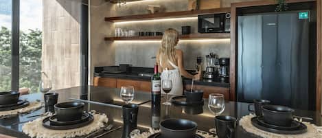 Une cuisine moderne dotée d’un îlot central, agrémentée de bols noirs et de verres à vin, et une femme qui prépare une boisson.