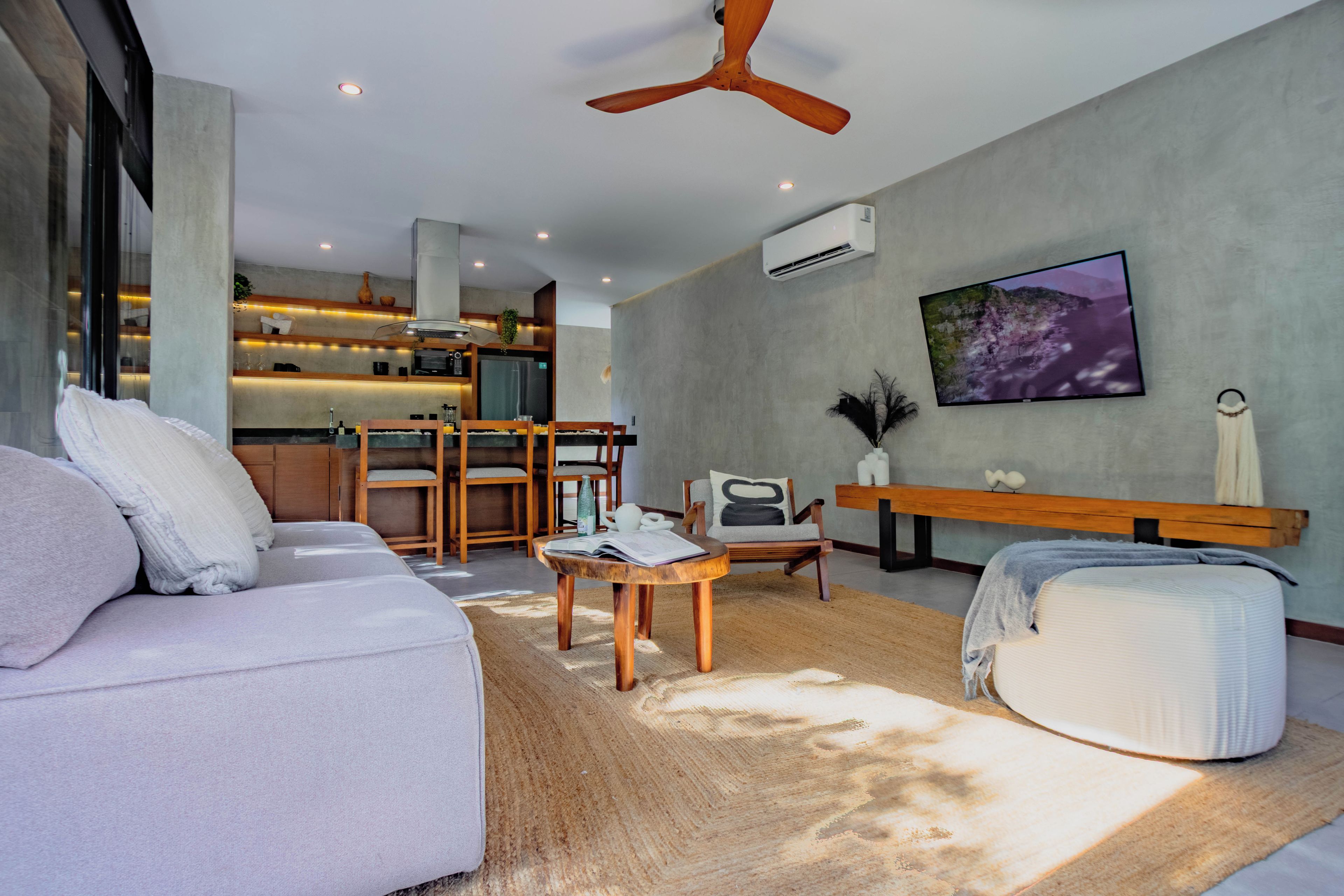 Una sala de estar moderna con un sofá, una mesa de centro y un televisor. Hay una zona de cocina con una mesa de comedor y sillas.