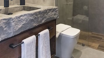 A modern bathroom with a marble sink, a wooden vanity, a glass shower enclosure, and a toilet.