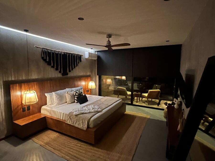 Un dormitorio moderno con una cama grande, lámparas de noche, ventilador de techo y vistas al exterior a través de una puerta de cristal.