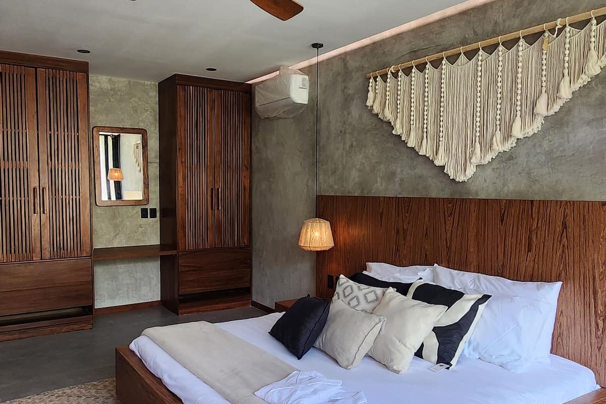 A spacious bedroom with a large bed, wooden headboard, a ceiling fan, and a woven rug.