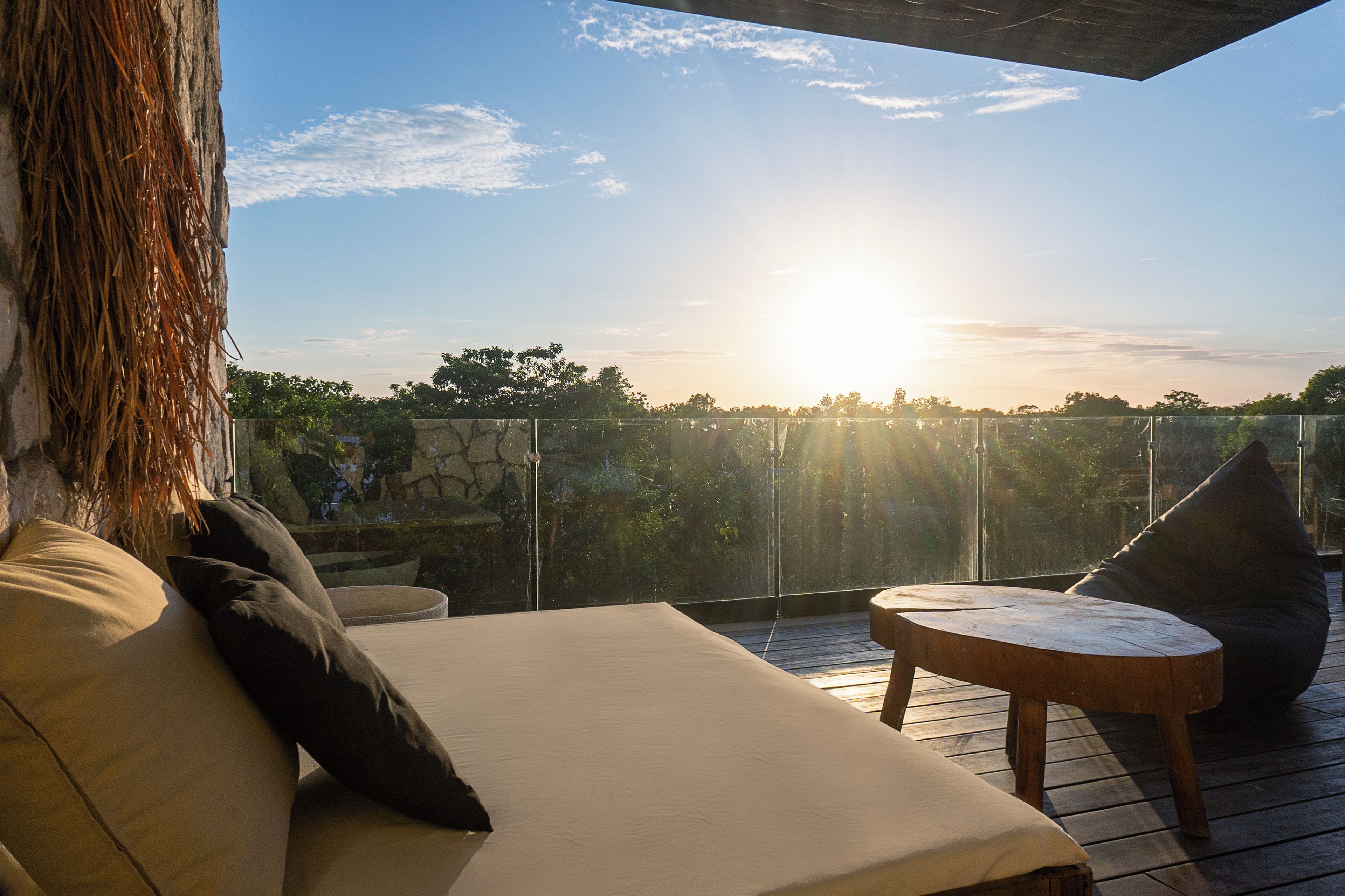 A balcony with a view of the sunset, a lounge chair, and a small table.