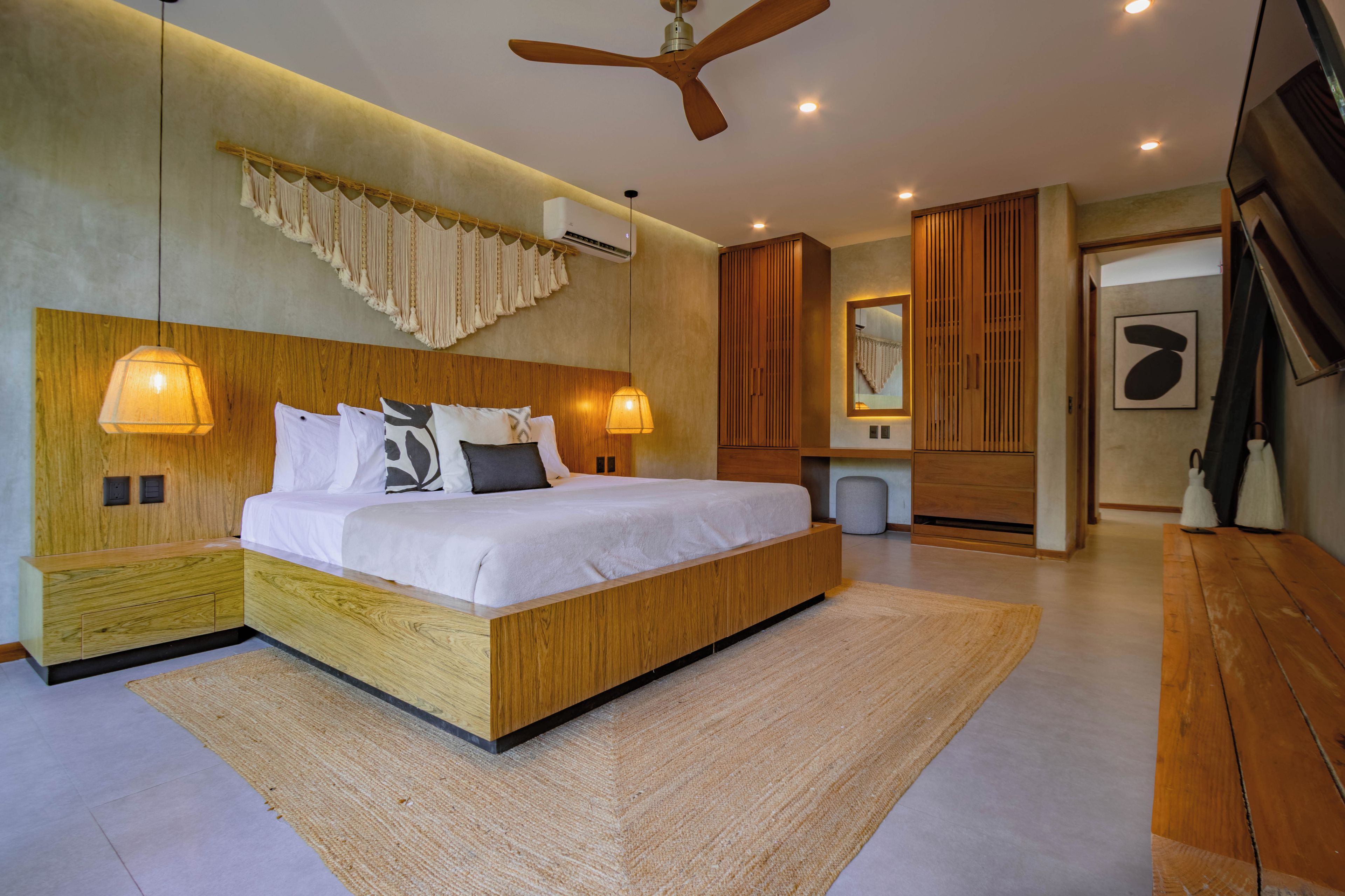 A modern bedroom with a large bed, wooden headboard, bedside lamps, and a ceiling fan.