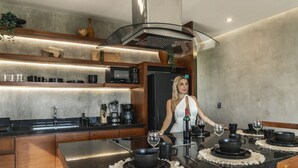 A modern kitchen with a central island, built-in appliances, and a dining area with black tableware. - Xambé  (Tulum)