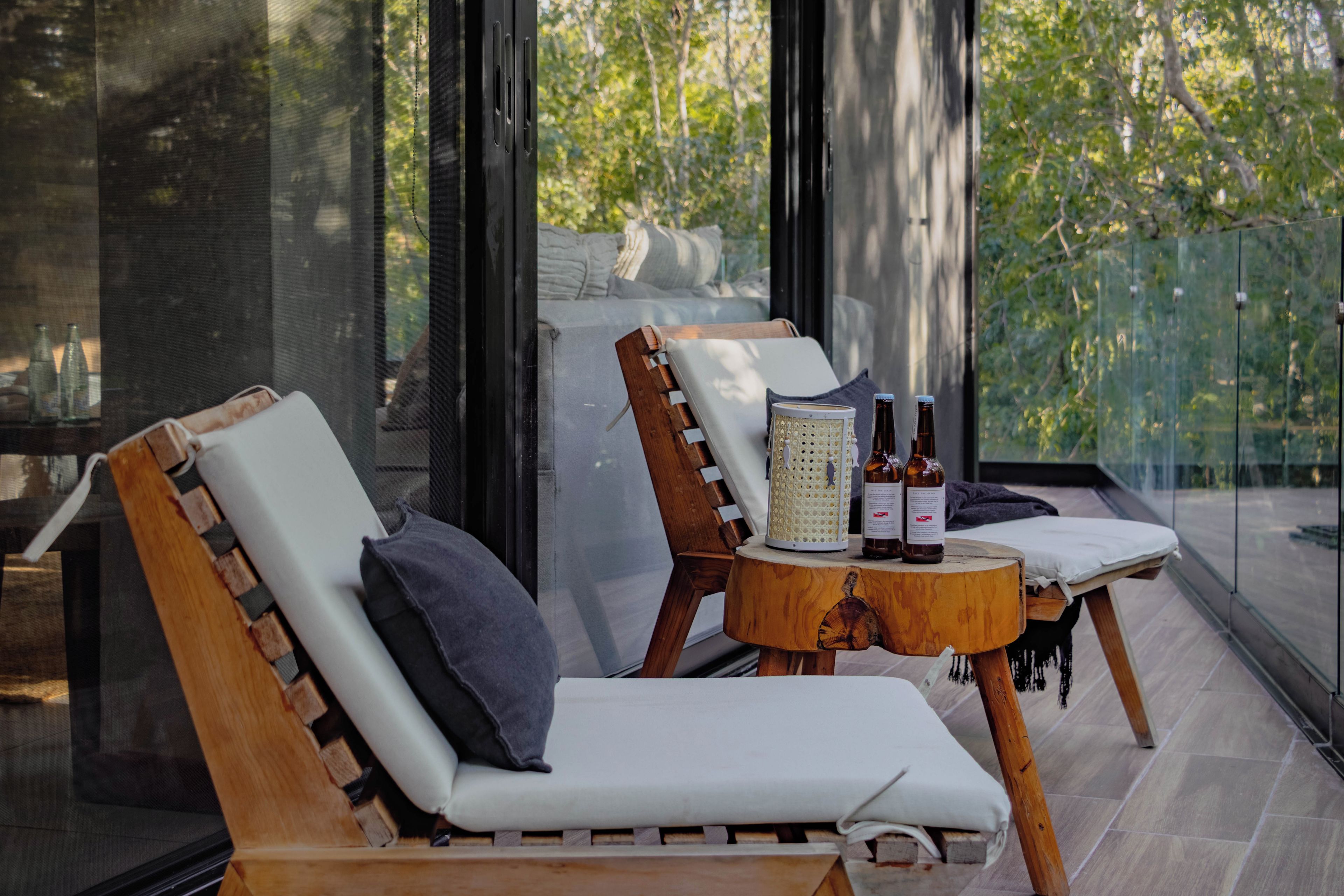 A modern lounge area with two wooden lounge chairs, a small wooden table with bottles, and a decorative lantern.