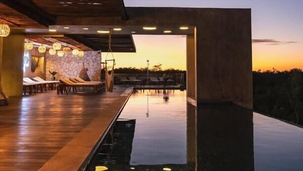 A modern outdoor pool area with a stone wall, lounge chairs, and a sunset view. - Xambé  (Tulum)