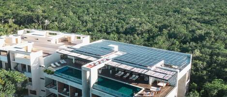 A modern hotel with multiple floors, rooftop solar panels, and a swimming pool.