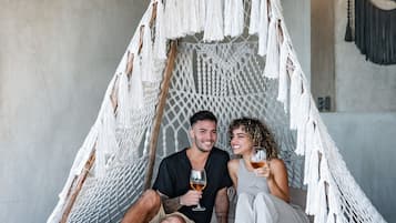 A couple sitting in a macrame hammock with a concrete floor and wooden ceiling.