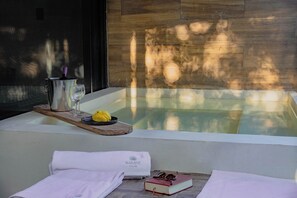 Un área de spa con una bañera, una bandeja de madera con una botella y vasos, toallas y un libro.