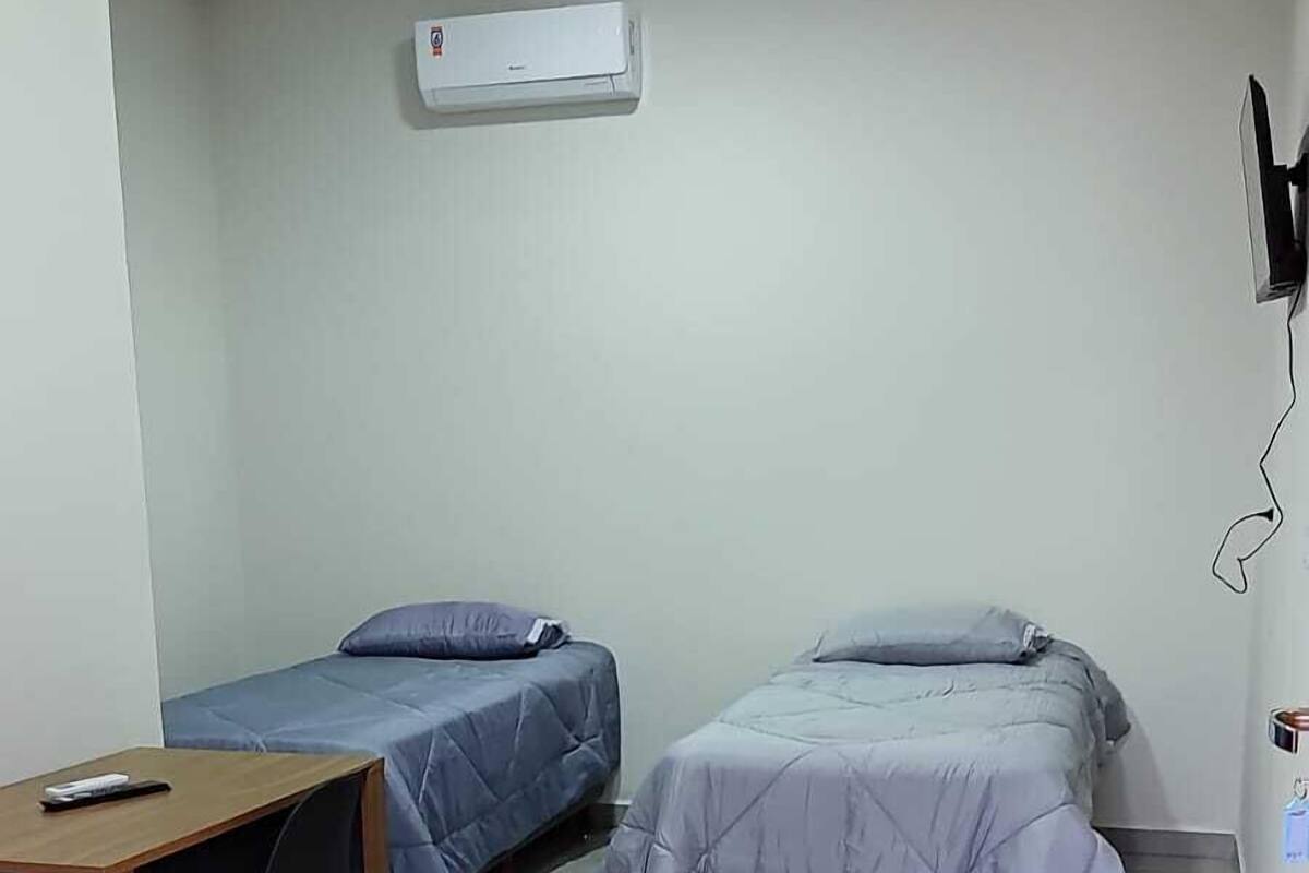 Una habitación pequeña y limpia con dos camas individuales, un escritorio y un equipo de aire acondicionado.