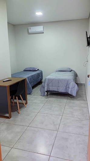 A small, clean room with two single beds, a desk, and an air conditioning unit. - Hotel Canoas (Tres Lagoas)