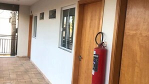 A corridor with tiled flooring, wooden doors, and a fire extinguisher mounted on one door. - Hotel Canoas (Tres Lagoas)