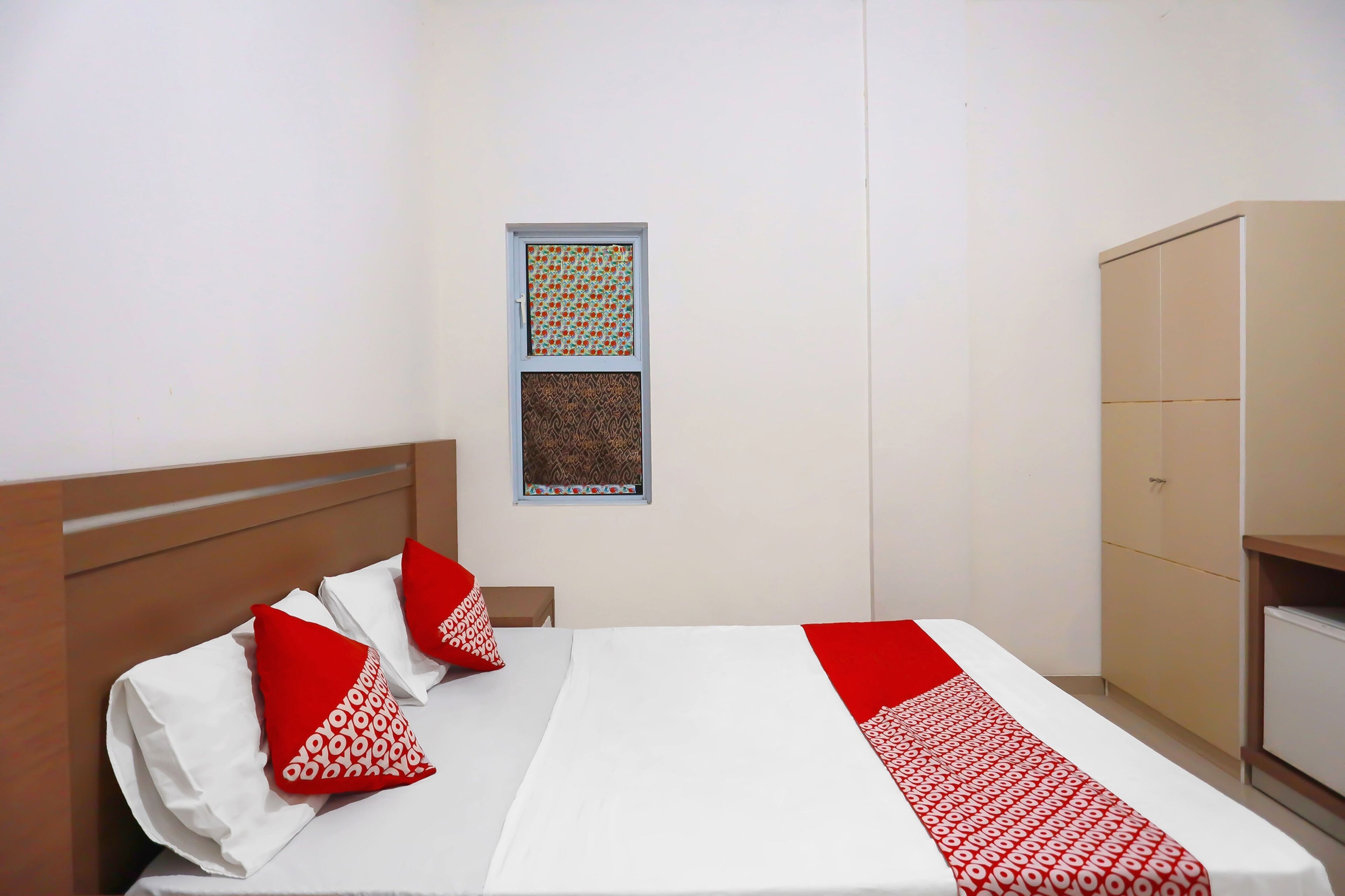A hotel room with a bed, pillows, a wardrobe, and two framed pictures on the wall.