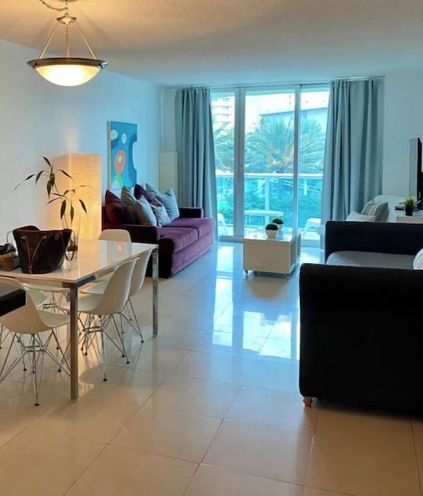 A modern living room with a dining area, large windows, and a view of the outdoors.