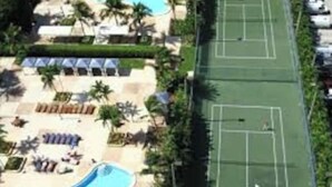 Oversigtsbillede af et resort med swimmingpool, tennisbaner og palmer.