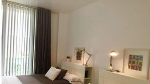 Et hotelværelse med to senge, et skrivebord med lampe, en lille reol med bøger og et vindue med gardiner.