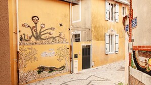 Une rue étroite bordée d’un immeuble jaune dont le mur est orné d’une fresque décorative.
