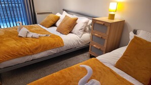 A hotel room with two beds, each with a brown blanket and a white towel folded on top. There is a wooden nightstand with a lamp on it. - Luxury River View 2-bed Apt, Wifi, Garden, River (Salford)