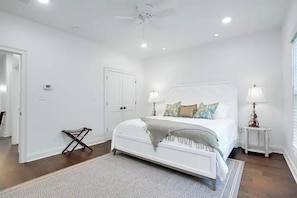 A bedroom with a white bed, two bedside tables with lamps, a ceiling fan, and a door.