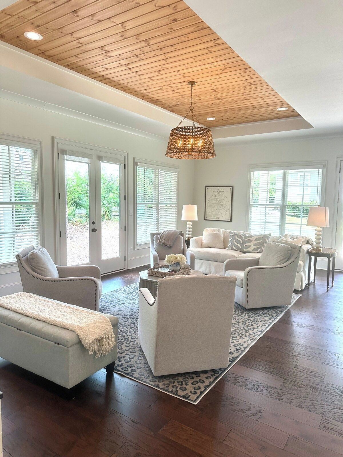 A spacious living room with a high ceiling, large windows, and a central chandelier.
