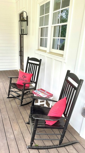 Two rocking chairs with red cushions on a wooden porch with white siding and a window.