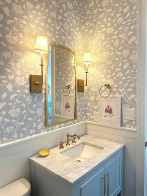 Un bagno con lavabo in marmo, accessori dorati e carta da parati floreale.