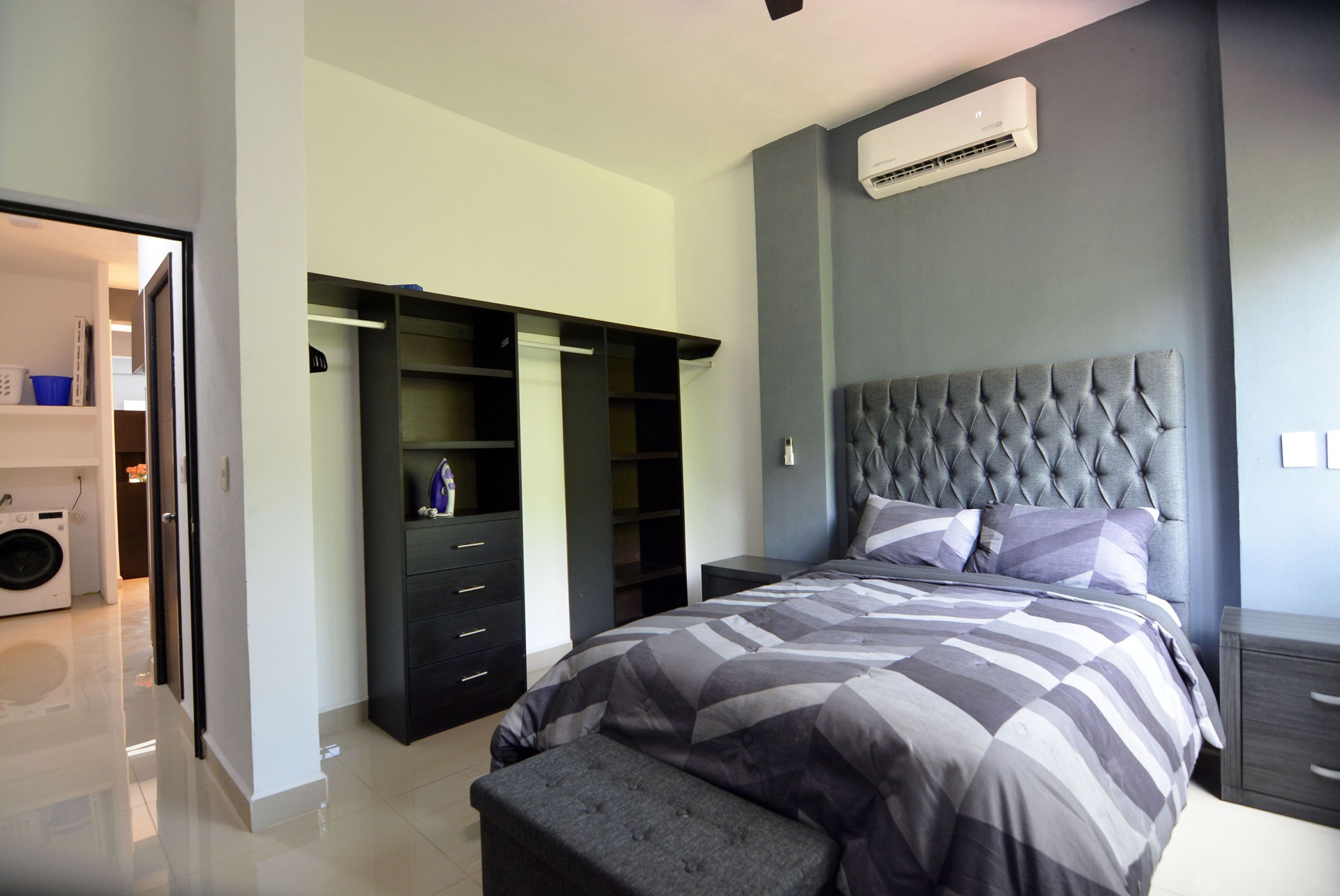 A bedroom with a large bed, a grey upholstered headboard, and a built-in wardrobe with multiple shelves.