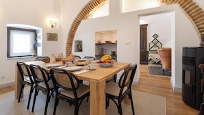 A dining area with a wooden table, black chairs, and a fruit bowl. - Casa Cordovil Evora (Évora)