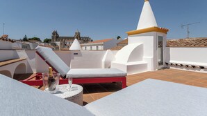 A rooftop terrace with white lounge chairs, a small table with a bottle and glass, and a white and yellow tower structure. - Casa Cordovil Evora (Évora)