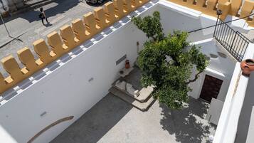An aerial view of a courtyard with a tree, a small staircase, and a white building with yellow railings.