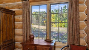 A log cabin room with a large window, a wooden dresser, a wicker chair, and a basket. - First Tracks on Sundance - Slope-side Skiing! Views - Private Hot Tub - A/C ! (Mountain Village)