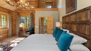 A log cabin bedroom with a large bed, a chandelier, wooden walls, and a view of the outdoors. - First Tracks on Sundance - Slope-side Skiing! Views - Private Hot Tub - A/C ! (Mountain Village)