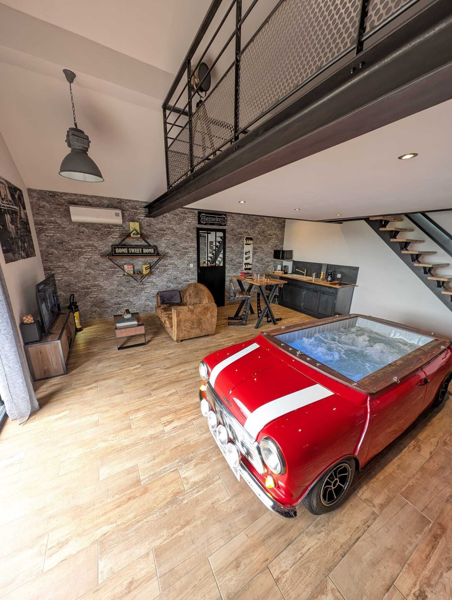 A spacious living area with a red vintage car, a wooden dining table, and a modern kitchen.