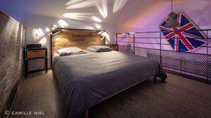 Une chambre avec une tête de lit en bois, un lit avec une literie grise, une table de chevet avec une lampe et un mur orné d’un motif Union Jack.