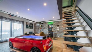 Un salon moderne avec une voiture rouge d’époque, une table de billard, un escalier et une enseigne Heineken.
