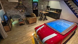 Un espace de vie moderne agrémenté d’une voiture ancienne rouge, d’une enseigne Heineken et d’un coin salon confortable.