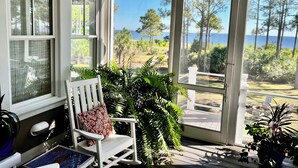 A covered porch with a rocking chair, a view of the ocean, and a patio area with chairs.