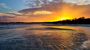 A beach with a sunset, calm waters, and a distant shoreline.
